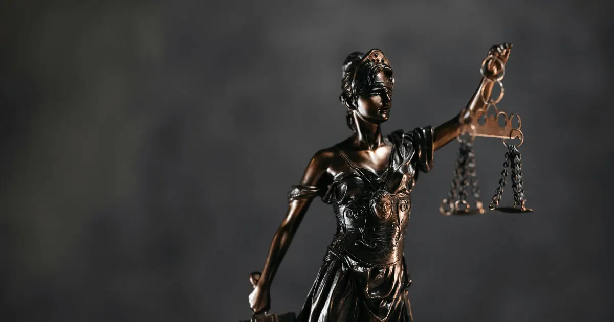 Estátua de bronze da Deusa da Justiça, Têmis, segurando uma balança e uma espada com um fundo escuro.